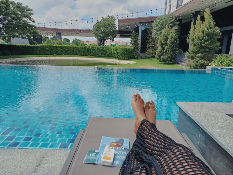 woman laying by a pool with book practicing self care